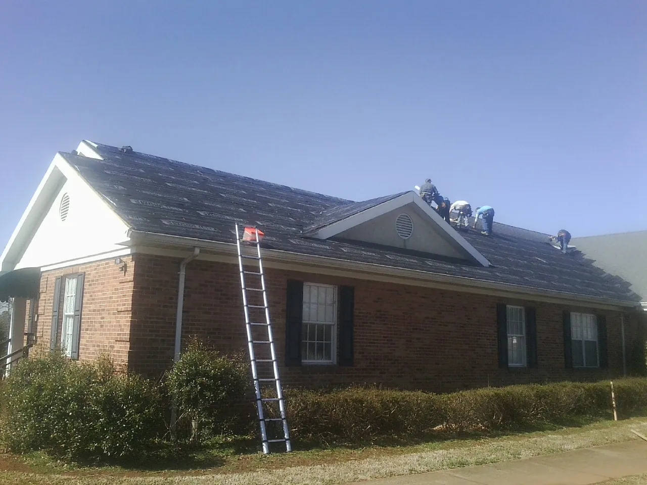 Crew tearing shingles off a brick ranch roof with a ladder set — Emergency Roof Repair work by our crew in Granite City