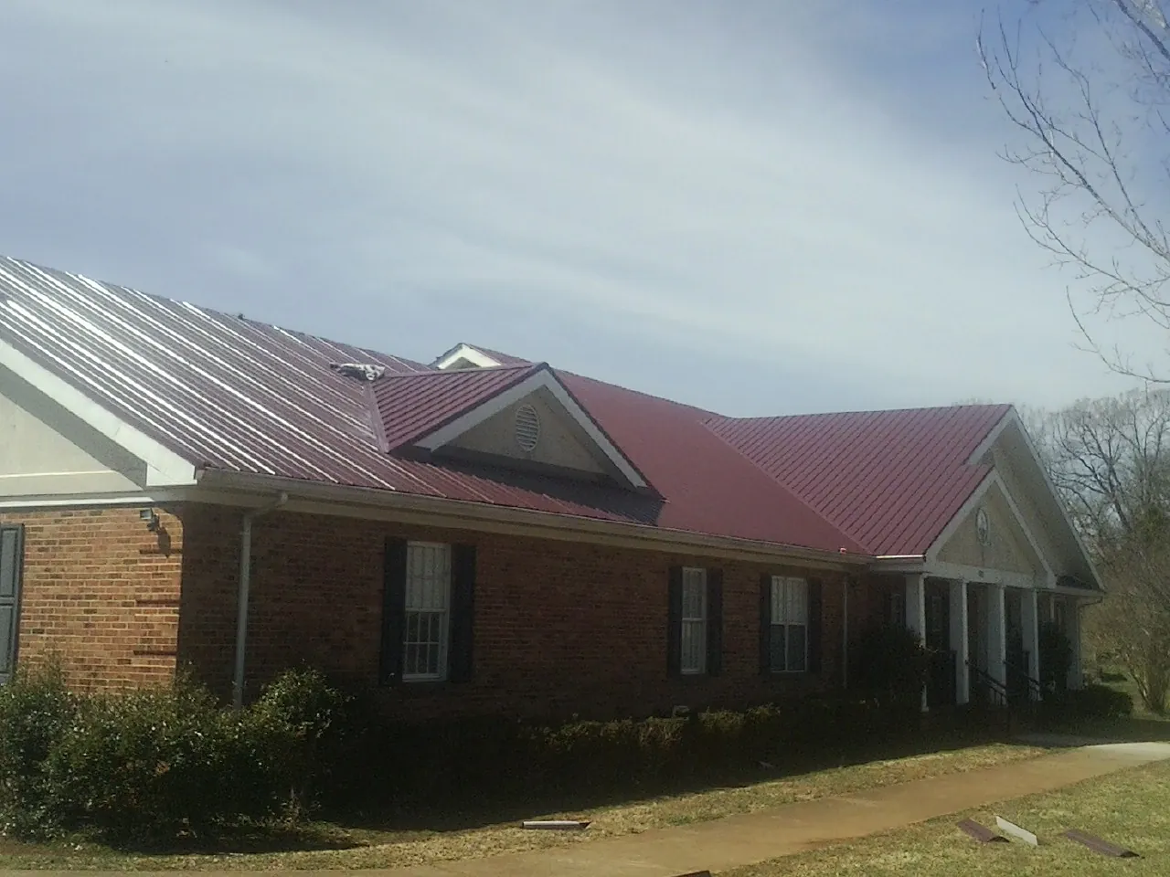 Red metal roof with gabled entries on a long brick building, from a Hail Damage Roof Repair job in Granite City