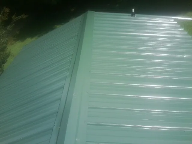 New green metal panels meeting at the ridge of a roof — Flat Roof Repair work by our crew in Granite City