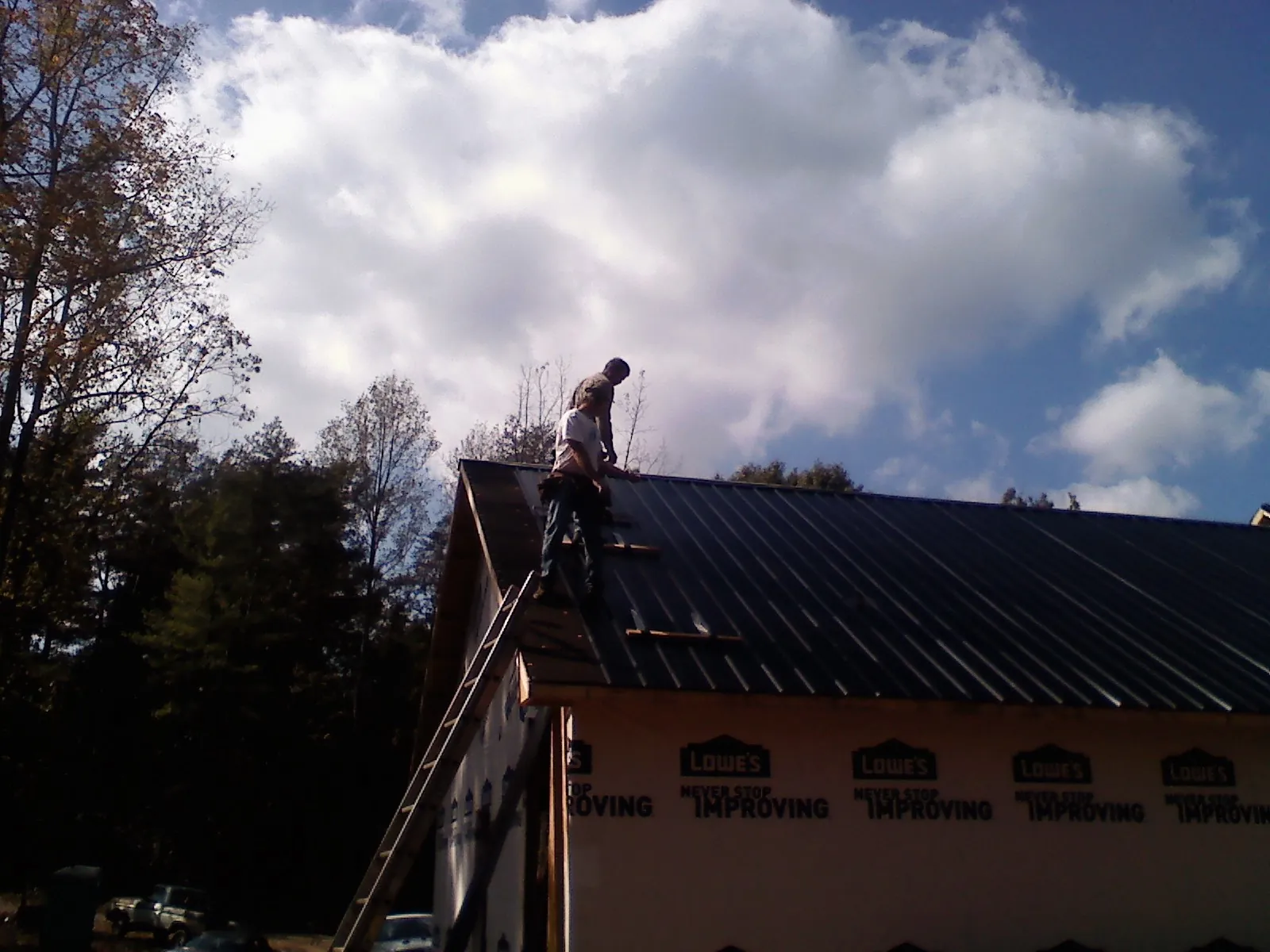 Roofer fastening dark metal panels high against a cloudy sky, from a Roof Inspection job in Granite City