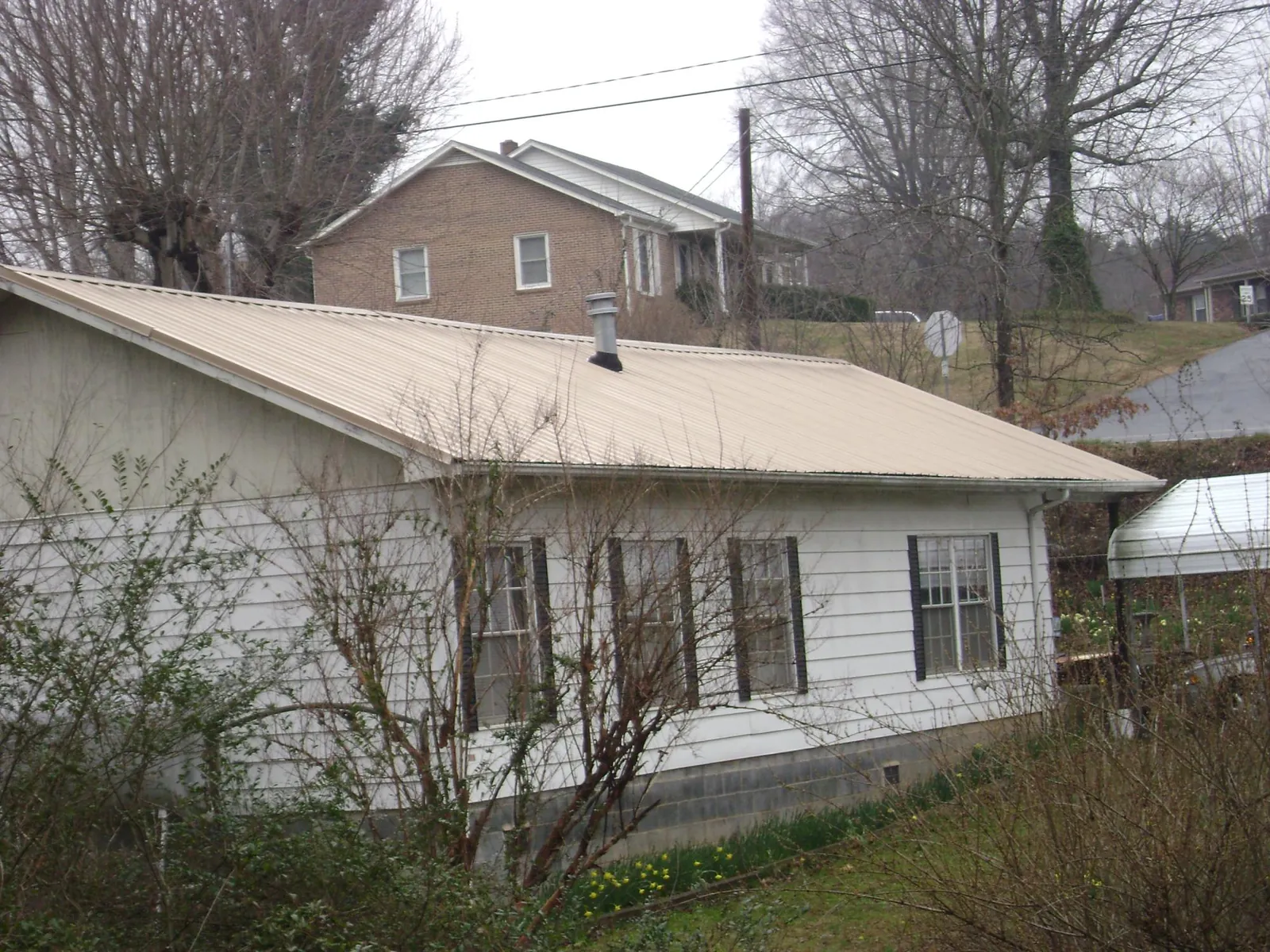 Tan metal roof on a white sided house set into a hillside — Commercial Roofing by Roofing Brothers in Granite City